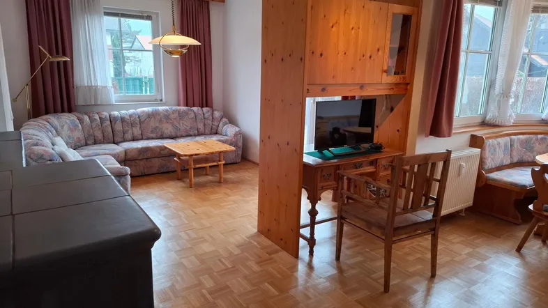 Gemütlicher Wohn- und Essbereich mit traditionellen Holzmöbeln, Parkettboden und Kachelofen.