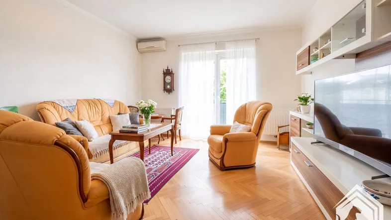 Helles Wohnzimmer mit bequemen Ledersofas, Parkettboden und Zugang zum Balkon.