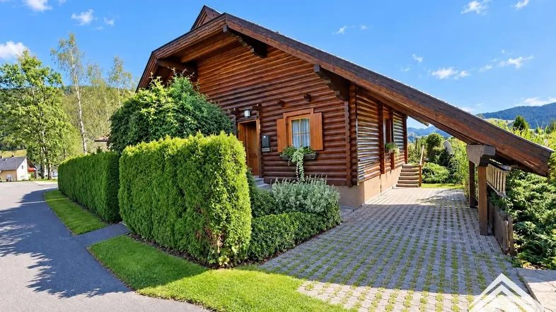 Charmantes Holzhaus mit gepflegtem Vorgarten und Zufahrt unter blauem Himmel.