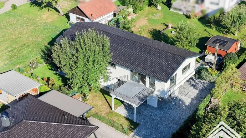 Luftaufnahme eines modernen Einfamilienhauses mit gepflasterter Auffahrt und großem Balkon.