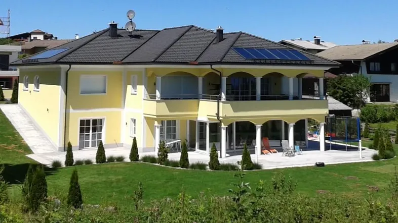 Großzügiges Einfamilienhaus mit gelber Fassade, Balkonen, Terrasse und Solaranlage auf dem Dach.