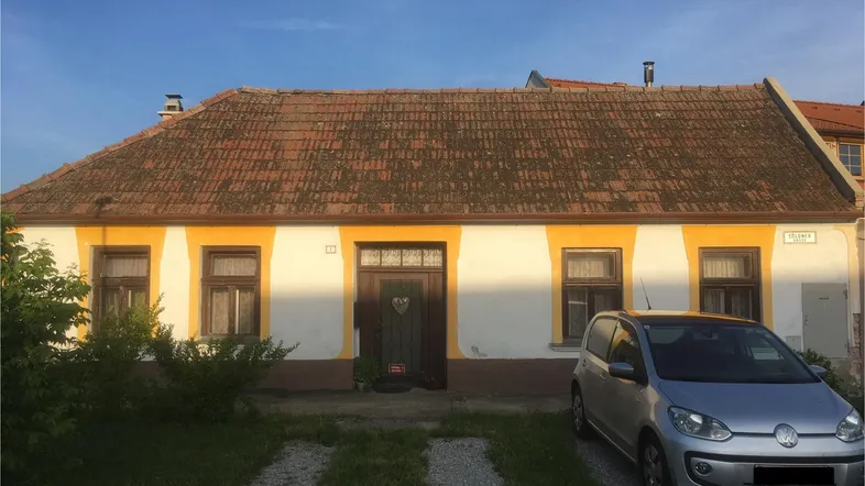 Altes Landhaus mit gelb umrandeten Fenstern und rotem Ziegeldach unter blauem Himmel.