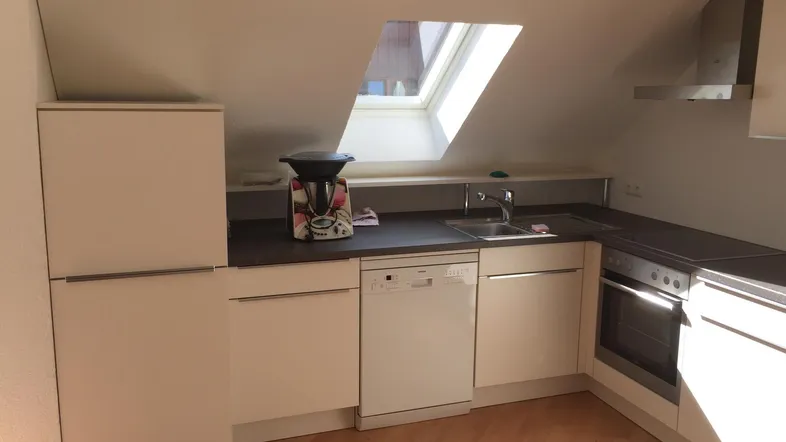Helle Küche im Dachgeschoss mit Einbaugeräten, Dachfenster und Holzfußboden.