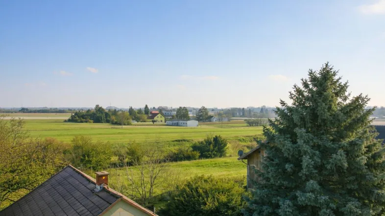 Weitläufiger Blick über grüne Felder und ländliche Umgebung unter blauem Himmel.