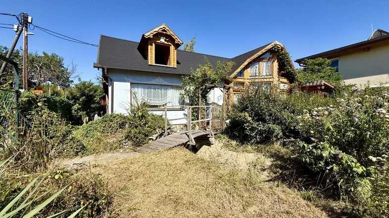 Charmantes Haus mit traditionellen Holzelementen und einem kleinen Steg im verwilderten Garten.
