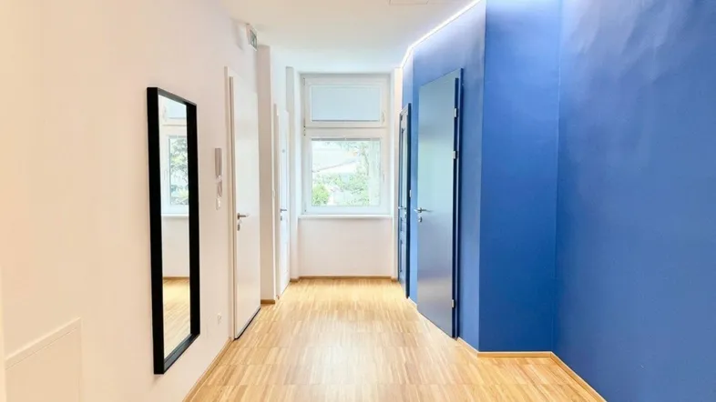 Moderner Flur mit blauer Akzentwand, hellem Holzfußboden und indirekter Deckenbeleuchtung, die den Raum erhellt.