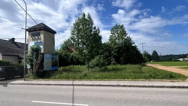 Grundstück an einer Straße mit Bäumen und einem Werbeplakat unter blauem Himmel.