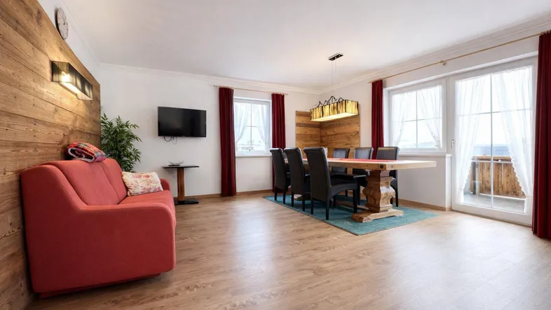 Geräumiger Wohn-Essbereich mit Holzakzenten, rotem Sofa und Zugang zum Balkon.