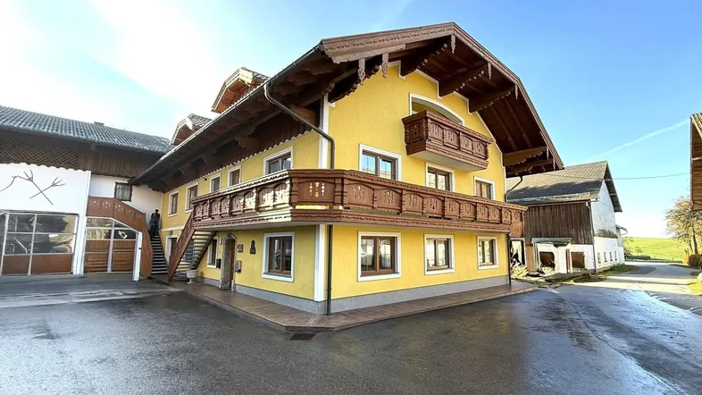 Traditionelles Bauernhaus mit gelber Fassade, geschnitzten Holzbalkonen und sonnigem Vorplatz.
