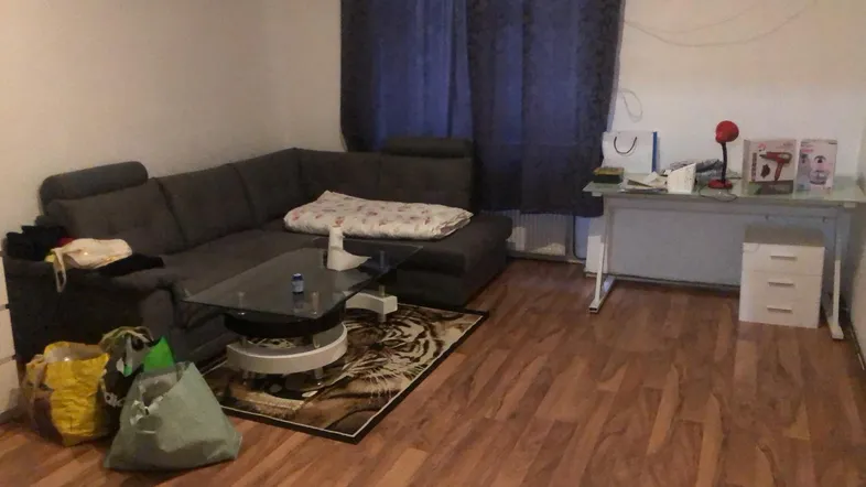 Gemütliches Wohnzimmer mit Ecksofa, Holzboden und einem kleinen Arbeitsbereich am Fenster.