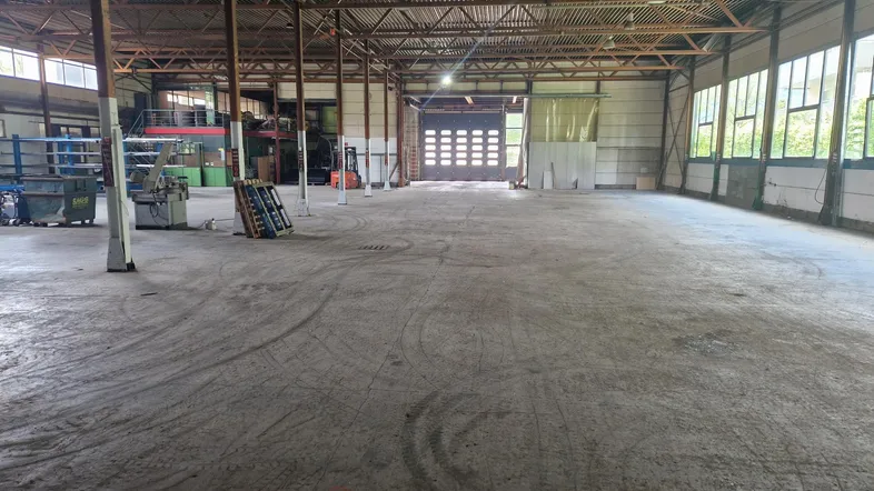 Geräumige Industriehalle mit hohen Decken, Betonboden und großem Rolltor am Ende des Raumes.