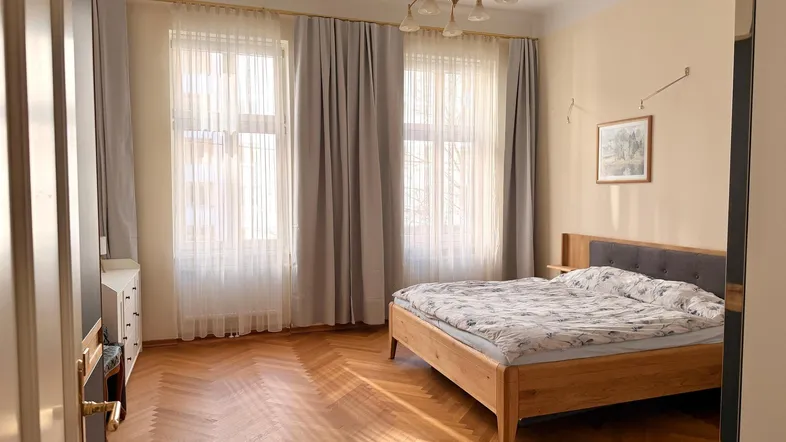 Helles Schlafzimmer mit elegantem Fischgrätparkett, großzügigen Fenstern und einem bequemen Doppelbett.