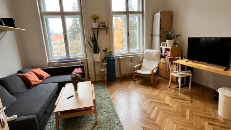 Helles Wohnzimmer mit Fischgrätparkettboden, bequemer Couch und großen Fenstern.