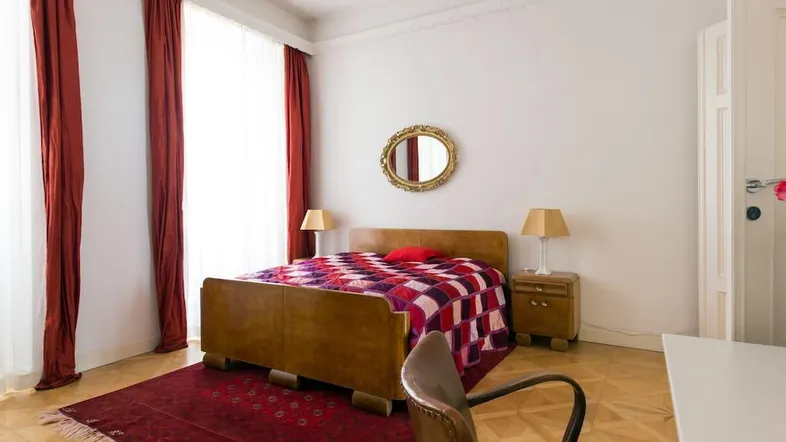 Helles Schlafzimmer mit Holzbett, roten Vorhängen und Parkettboden, klassisch eingerichtet.