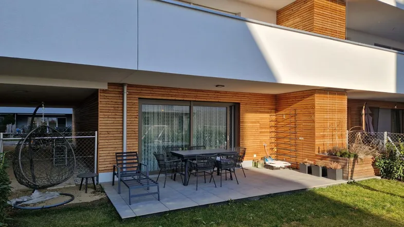 Moderne Terrasse mit Gartenmöbeln und Zugang zum privaten Gartenbereich eines Neubaus.