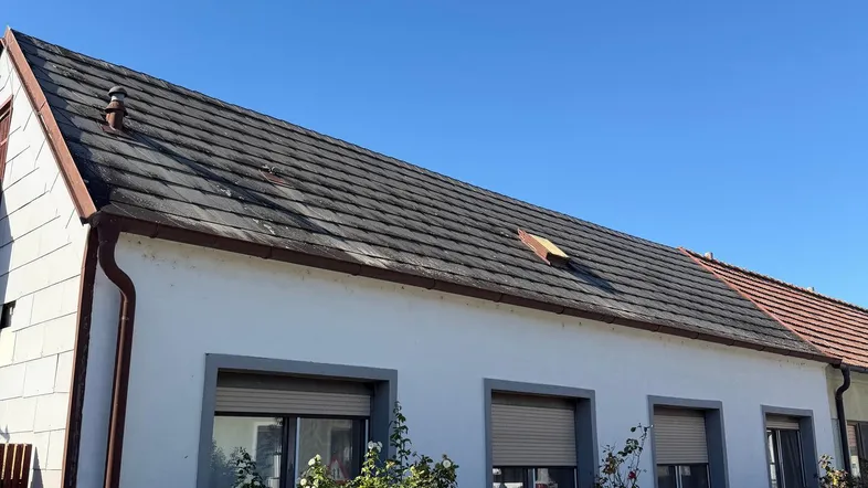 Fassade eines Einfamilienhauses mit Satteldach und Rollläden unter blauem Himmel.