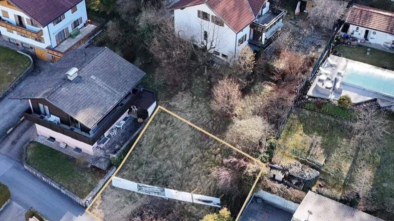 Luftaufnahme eines Baugrundstücks in einer Wohngegend mit umliegenden Häusern und Vegetation.