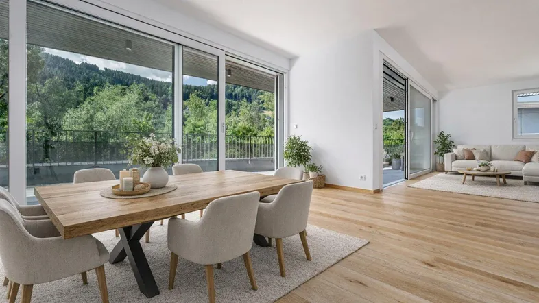Heller, offener Wohn- und Essbereich mit Holztisch, bequemen Stühlen und Zugang zur Terrasse mit Bergblick.