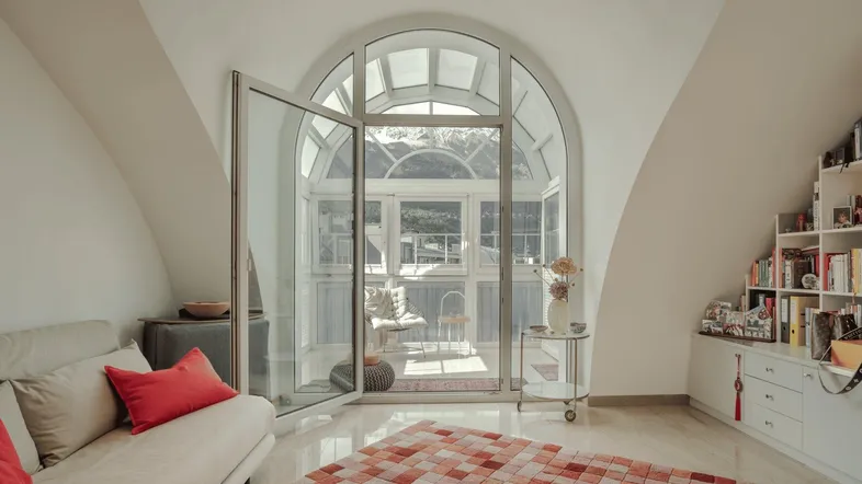 Heller Wohnbereich mit großer gewölbter Glasfassade, die zu einem Wintergarten oder einer Loggia führt.