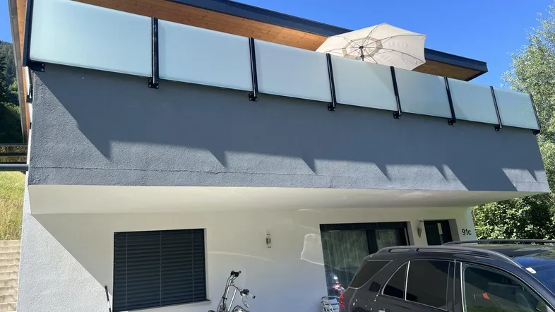 Moderne Hausfassade mit Balkon, davor ein Auto und ein Motorrad geparkt.