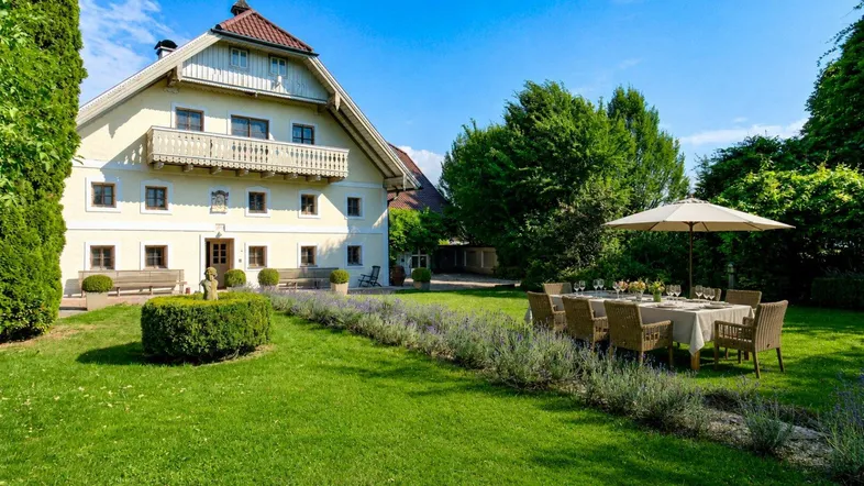 Traditionelles Landhaus mit großem Garten, Essbereich im Freien und gepflegter Rasenfläche unter blauem Himmel.
