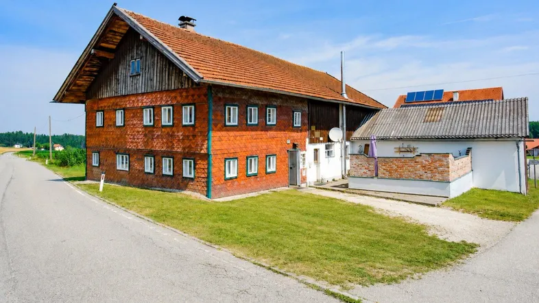 Traditionelles Bauernhaus mit rotem Ziegeldach und Holzfassade in ländlicher Umgebung.