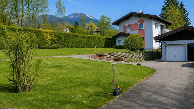 Großzügiger Vorgarten mit gepflegtem Rasen, Auffahrt und Blick auf die umliegende Berglandschaft.
