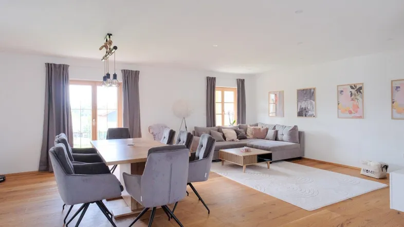 Helles, offenes Wohn-Esszimmer mit Holzboden, großem Esstisch und gemütlichem Sofa.
