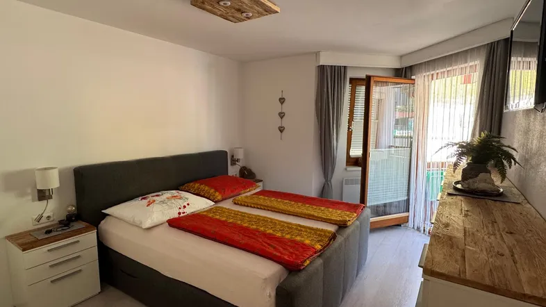 Helles Schlafzimmer mit Doppelbett, Holzmöbeln und direktem Zugang zum Balkon.