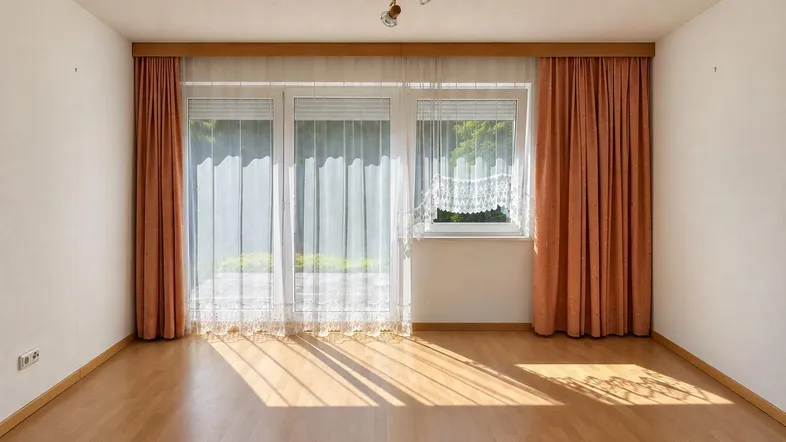 Helles Wohnzimmer mit Parkettboden und Zugang zu einem kleinen Außenbereich, gut beleuchtet durch große Fenster.