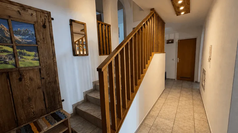 Heller Flur mit Holztreppe und rustikalen Holzelementen, der zu den oberen Etagen führt.