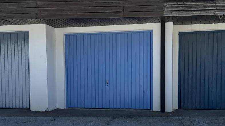 Nahaufnahme einer blauen Garagentür mit weißem Rahmen und Holzelementen darüber.