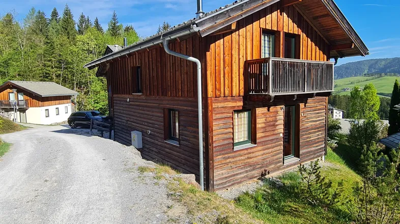 Rustikales Holzhaus im alpinen Stil mit Balkon und umgeben von grüner Natur.