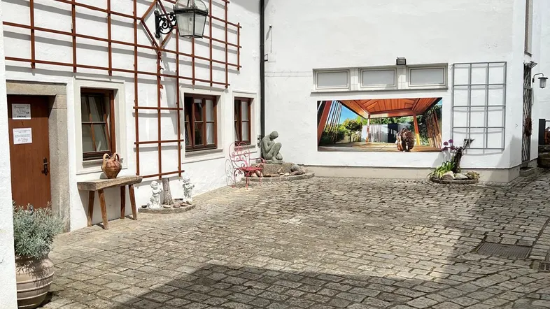Gepflasterter Innenhof mit weißen Gebäudefassaden, dekorativen Rankgittern und einem großen Wandbild.