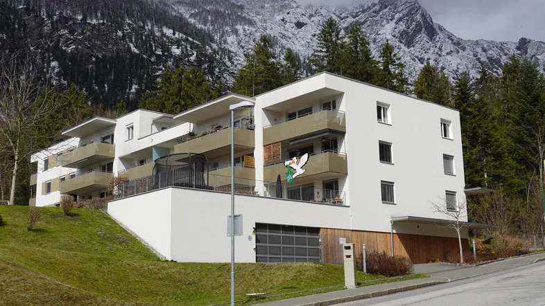 Modernes Mehrfamilienhaus mit Balkonen und Bergblick in alpiner Umgebung.