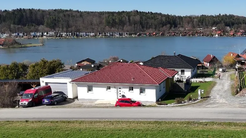 Einfamilienhaus mit rotem Ziegeldach und Seeblick in ländlicher Umgebung.