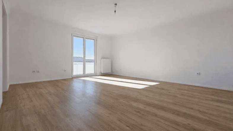 Helles Wohnzimmer mit neuem Laminatboden und Zugang zu einem Balkon, durchflutet von natürlichem Licht.