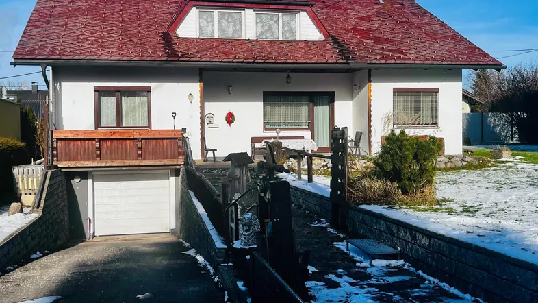 Einfamilienhaus mit rotem Dach, weißer Fassade, Garage und verschneitem Vorgarten an einem sonnigen Tag.