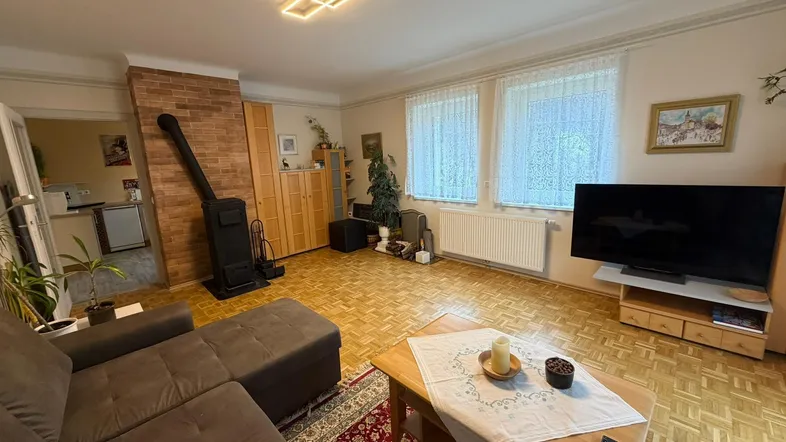 Gemütliches Wohnzimmer mit Parkettboden, Kaminofen und Blick ins Grüne durch die Fenster.