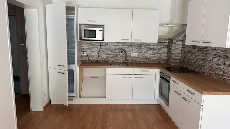 Moderne Einbauküche mit weißen Schränken, Holz-Arbeitsplatte und integrierten Geräten.