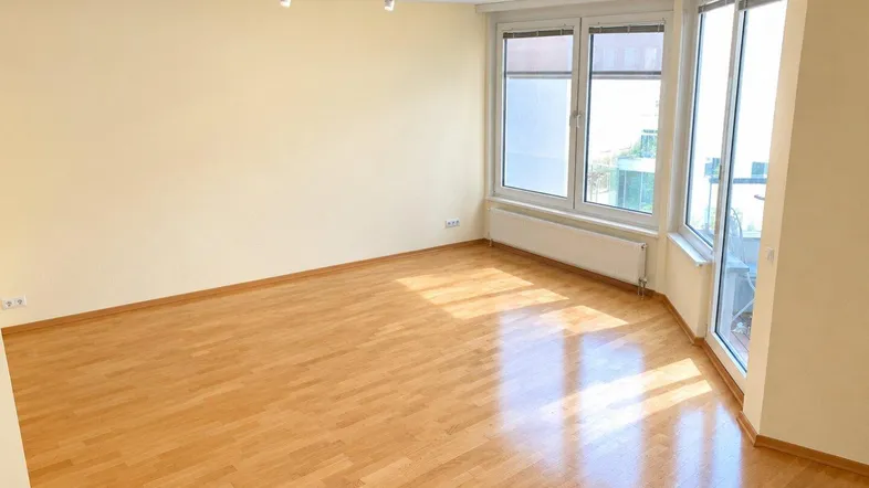 Helles, unmöbliertes Wohnzimmer mit Parkettboden und Zugang zum Balkon, ideal für individuelle Gestaltung.