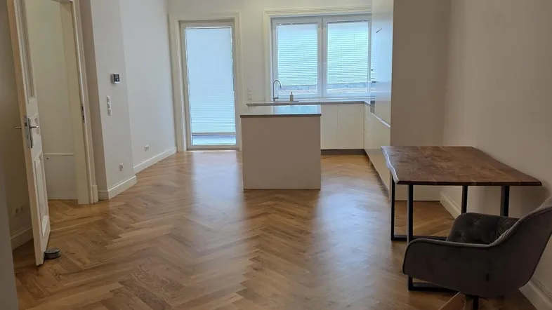 Heller offener Wohnbereich mit Fischgrätparkett und integrierter moderner Küche sowie Zugang zum Balkon.