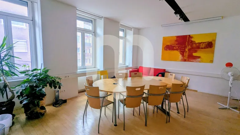 Heller Konferenzraum mit großem ovalen Holztisch, vielen Stühlen und großen Fenstern, ideal für Besprechungen.