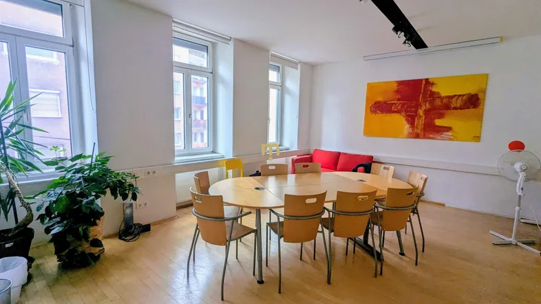 Heller Besprechungsraum mit großem ovalen Tisch, Holzfußboden und mehreren Fenstern.