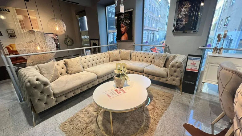 Großes Ecksofa in beigem Samt mit Chesterfield-Steppung und Couchtischen in einem modernen Ausstellungsraum.