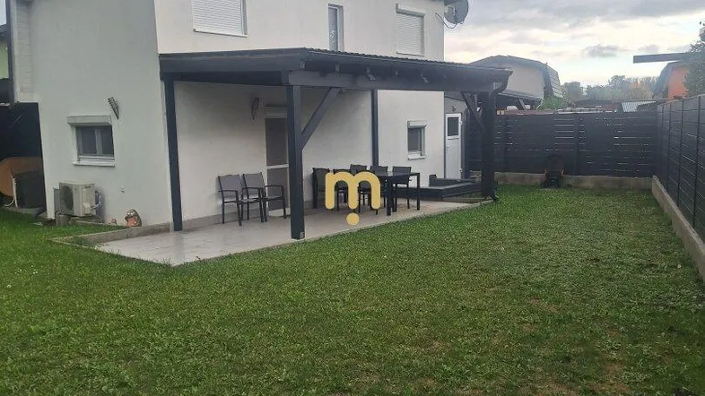 Modernes Haus mit überdachter Terrasse, Gartenmöbeln und großem Rasenbereich.