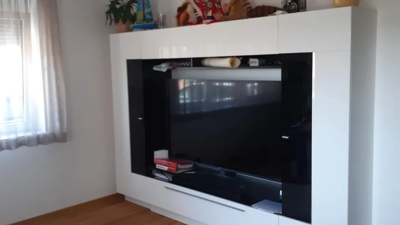 Helles Wohnzimmer mit modernem TV-Möbel, Holzboden und einem Fenster mit Vorhängen.