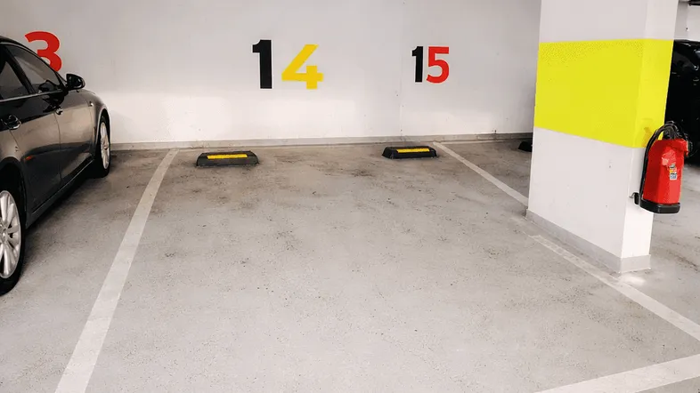 Tiefgarage mit markierten Stellplätzen, Brandschutzvorrichtung und sichtbaren Leitungen an der Decke.