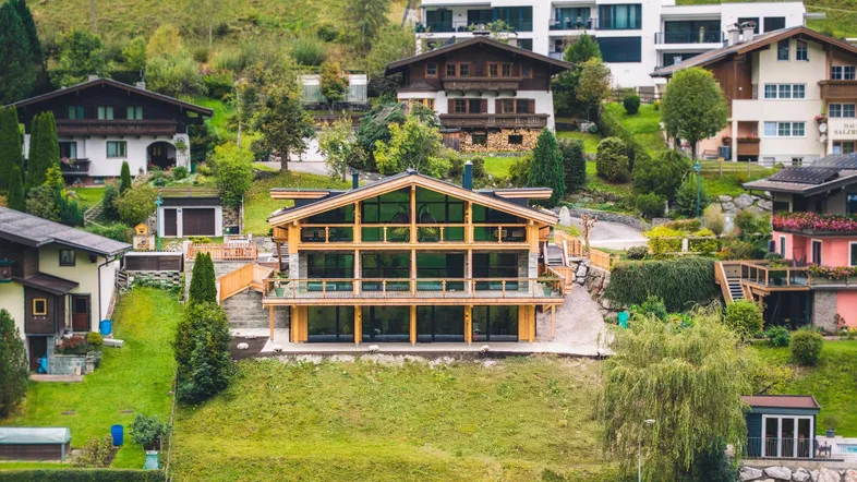 Modernes Holzhaus mit großen Glasfronten in alpiner Hanglage umgeben von weiteren Häusern.