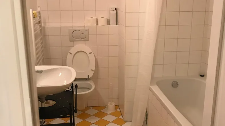 Badezimmer mit Badewanne, Toilette und Waschbecken, gekennzeichnet durch gelb-weiß karierte Fliesen und gelbe Akzente.